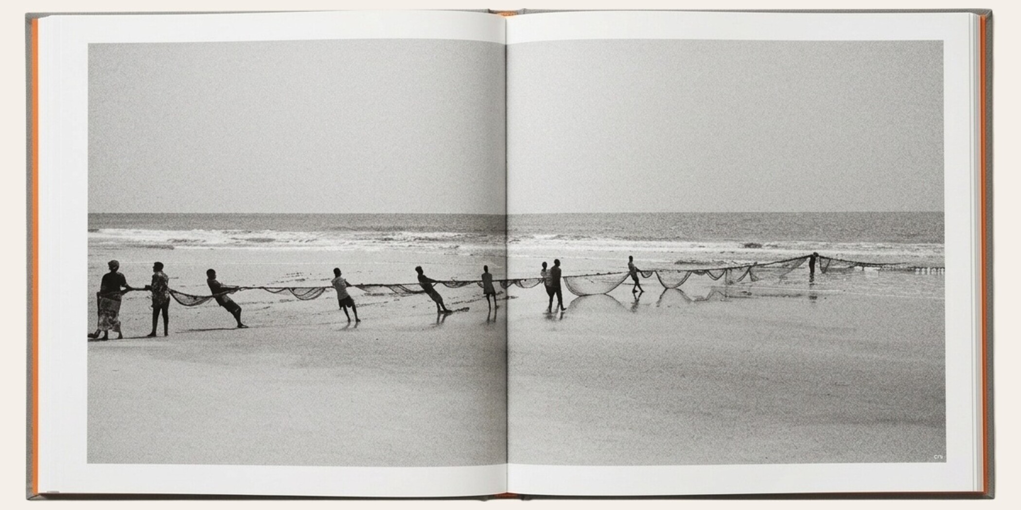 The Matriarch's Line opened flat to spread 074 — a wide black-and-white photograph of a line of people pulling a seine net at the water's edge, running across both pages. Gray Cialux cloth cover with Sirio Arancio orange endpapers visible at the outer edges.